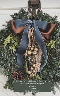 a christmas wreath hanging on the front door with a blue ribbon and bells attached to it