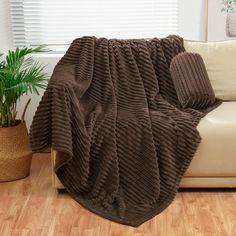 a brown blanket sitting on top of a couch next to a potted plant