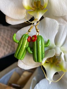 a pair of green cactus earrings hanging from a white flower with red berries on it