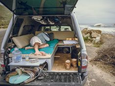 a man sleeping in the back of a van with its bed pulled up to it