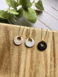 three different necklaces sitting on top of a wooden table next to a potted plant