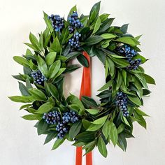 a wreath with blue berries and green leaves hangs on the wall next to an orange pair of scissors