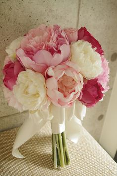 a bridal bouquet with pink and white peonies on a chair in front of a wall