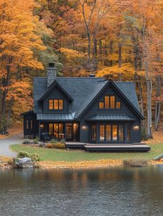 a black house sitting on top of a lake surrounded by fall foliage and trees in the background