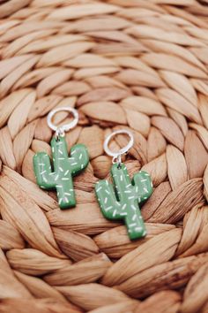 two green cactus shaped earrings sitting on top of a woven basket next to each other