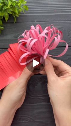 someone is making a paper flower out of red construction paper and some pink ribbon on top