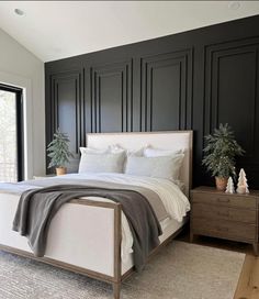 a bedroom with black paneled walls, white bedding and two potted plants