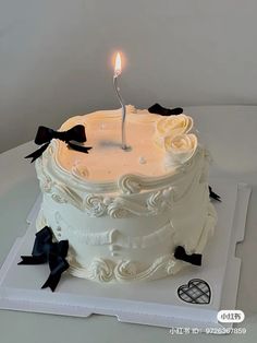 a white cake sitting on top of a table with a lit candle in the middle