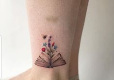 an open book with flowers and butterflies on its cover - up tattoo is shown in front of a woman's leg