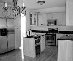 a black and white photo of a kitchen with stainless steel refrigerator, stove, oven, sink, and chandelier