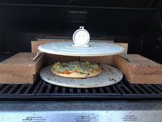 a pizza sitting on top of an open grill with a clock in the back ground