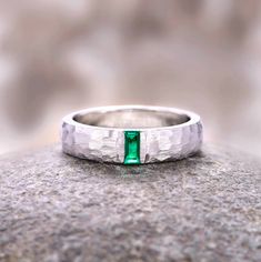 a white gold ring with a green stone in the center on top of a rock