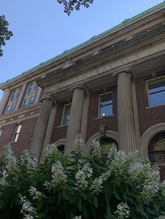 an old brick building with columns and flowers in the foreground, against a blue sky