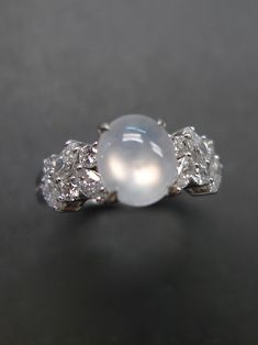 a white pearl and diamond ring on a gray surface with the center stone surrounded by smaller diamonds