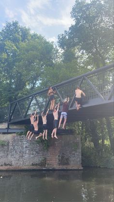 four men are hanging upside down on a bridge over a river and one man is jumping into the water with his arms in the air