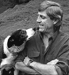 a man holding a dog in his lap while sitting on top of a grass covered field