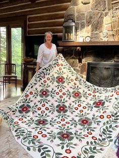 a woman standing next to a large quilt in front of a fire place with a fireplace