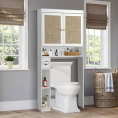 a white toilet sitting next to a tall cabinet in a bathroom with windows above it