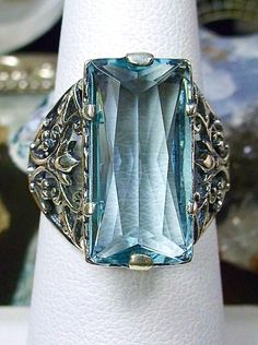 Sky Blue Aquamarine Ring Baguette Design#32 Introducing the Baguette D32, a stunning piece of wearable art that pays homage to the opulent Victorian era. Crafted with meticulous attention to detail, this exquisite filigree Antique reproduction in sterling silver is sure to captivate anyone with a love for vintage-inspired jewelry. At its center, lies a flawless 7ct sky blue gemstone, radiating a dazzling hue that catches the light with every movement. The baguette rectangle-cut gemstone measures Rectangular Aquamarine Jewelry For Wedding, Rectangular Aquamarine Blue Jewelry, Rectangular Aquamarine Wedding Jewelry, Rectangular Blue Aquamarine Jewelry, Blue Rectangular Aquamarine Jewelry, Elegant Aquamarine Blue Jewelry, Elegant Blue Aquamarine Jewelry, Rectangular Light Blue Jewelry Gift, Elegant Aquamarine Rectangular Jewelry