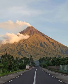 an empty road with a large mountain in the background and clouds coming from behind it