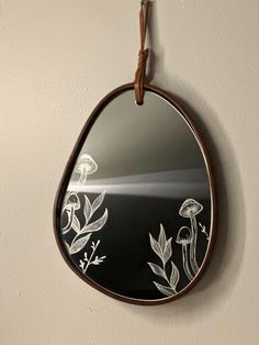 a mirror hanging on the wall with flowers painted on it and leather cord in front