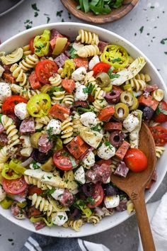 a bowl filled with pasta salad next to a wooden spoon