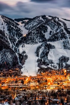 the town is nestled in the mountains with snow on it's sides and lit up at night