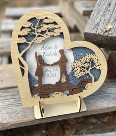 a wooden heart shaped with a couple holding hands on top of a bench next to a tree