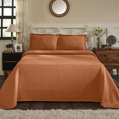 an orange bedspread and pillows in a bedroom with a mirror on the wall