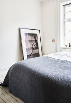 a bed in a white room with a black and white photo hanging on the wall