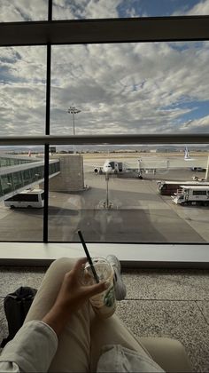 a person sitting in front of an airport window holding a cup and looking out the window