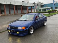 a blue car parked in front of a building on a wet street with no one around