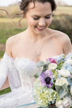 a woman in a wedding dress holding a bouquet of flowers and smiling at the camera