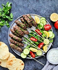 several skewers of meat and vegetables on a plate with pita bread