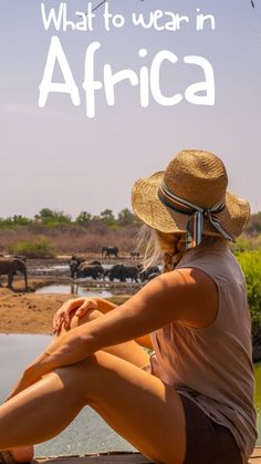 a woman sitting on the edge of a body of water with elephants in the background