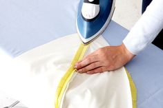 a person ironing fabric on an ironing board with a blue and white cover