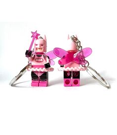 two pink legos are attached to each other on a white background, one is holding a cup and the other has a pair of scissors in it's hands