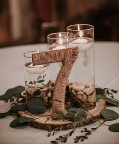 the table is set with candles, rocks and greenery in glass vases that spell out the number one