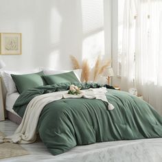 a bed with green sheets and pillows in a white room next to a window filled with plants