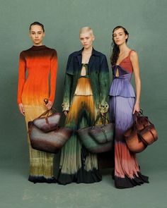 three models in long dresses with handbags and purses on their feet, standing next to each other