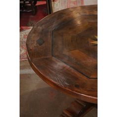 a round wooden table sitting on top of a floor next to a chair and rug