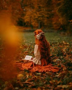 a woman sitting on top of a blanket in the middle of a forest reading a book