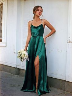 a woman in a green dress standing next to a wall with her hands on her hips