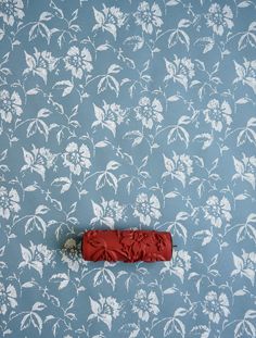 a red object laying on the ground in front of a blue floral wallpaper pattern