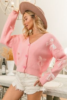 Add a touch of femininity to your wardrobe with our Pink Bow Detail Cardigan Sweater. Made from a pillowy soft knit, this button-down sweater features delicate white bow accents for a charming touch. Stay cozy and stylish in this must-have piece. Details: V-neck Long sleeves Button front closure Soft knit Ribbed Cuff 45% Acrylic | 25% Nylon | 30% Polyester Blend Fits TTS Imported Model Info: Model measures 34" | 23" | 36". Model is wearing a size small. Care: Hand wash cold water. Lay flat to dr Long Sleeve Fall Sweater With Bow, Long Sleeve Sweater With Bow For Fall, Fall Sweater With Bow And Long Sleeves, Spring Long Sleeve Sweater With Bow, Long Sleeve Sweater With Bow For Spring, Feminine Fall Cardigan With Buttons, Feminine Long Sleeve Cardigan With Button Closure, Cute Button-up Cardigan For Fall, Cute Button-up Fall Cardigan