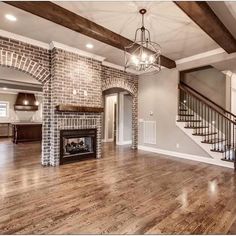 an empty living room with wood flooring and brick fireplace in the middle of it