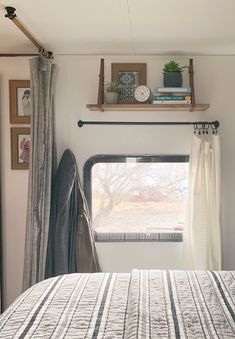 a bed sitting next to a window with curtains on top of it and a shelf above the bed