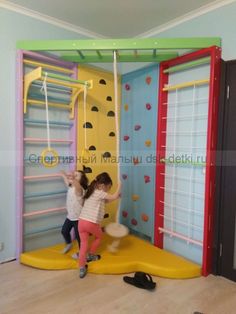 two children playing in a play room with climbing ropes and ladders on the walls