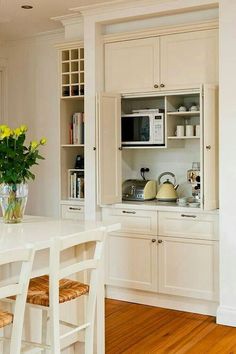 a kitchen with white cabinets and wooden floors is pictured in this image, there are yellow flowers on the counter