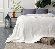 a bed with white linens and pillows in a bedroom next to a potted plant